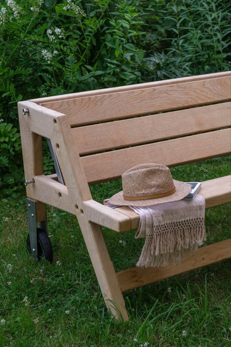 Banc en bois massif b-convivio installé dans un jardin, avec chapeau de paille et plaid