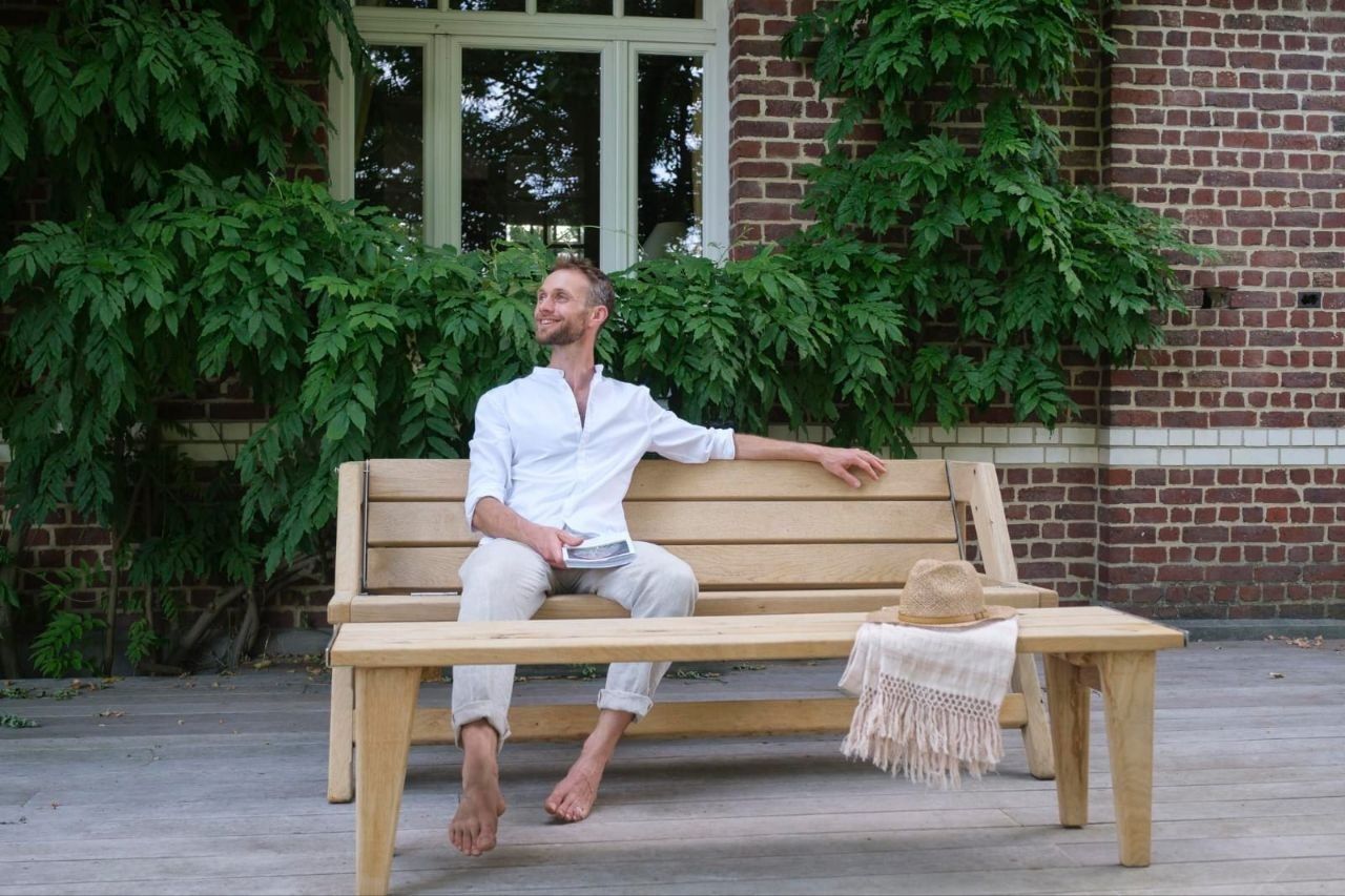Homme souriant, livre à la main, installé sur le mobilier b-convivio en terrasse